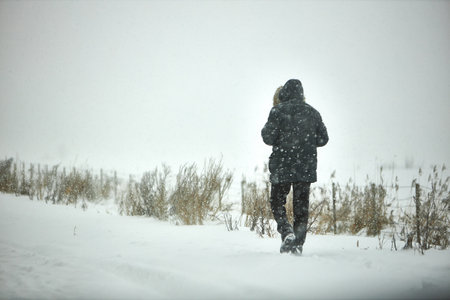 Person Walking in Snowy Field During Winter Snowstormの写真素材