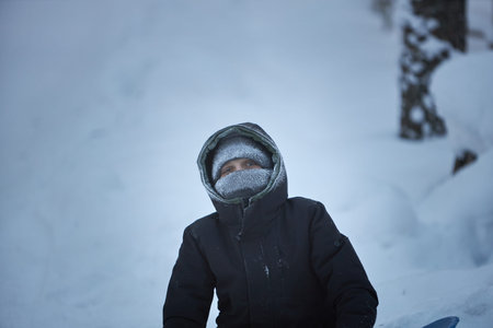 Young Boy Sitting in Snow With Snowboard
