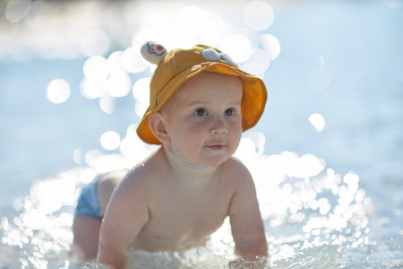 a little half a year old, a baby baby crawling on the water, smiling, outdoors, in a panama hat, in diapers, in the sun at the resort.の写真素材
