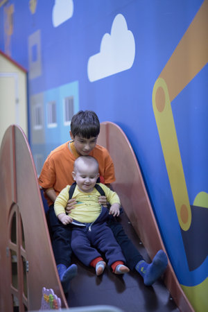 a one-year-old child with an older brother, riding a slide indoorsの写真素材