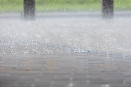 Heavy rain pouring onto a brick pathway in a green park during an afternoon downpourの写真素材