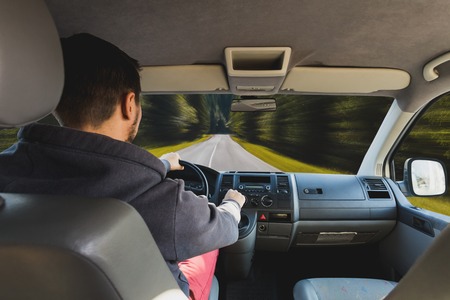 Hands of a driver on steering wheel of a car and empty asphalt roadの写真素材