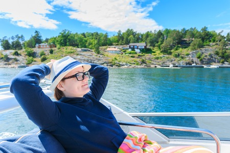 Relaxed girl with closed eyes of pleasure sitting on sailboat, enjoying mild sunlight, fashion model in luxury sea cruise, summer vacation and travelの写真素材