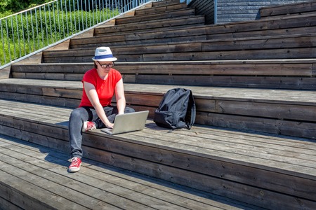 Smiling girl with glasses lying on the wooden stairs and using laptop and typingの写真素材