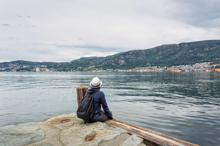 Girl wearing jeans and hat sitting on old wooden bridge at Bergen, Norwayの写真素材