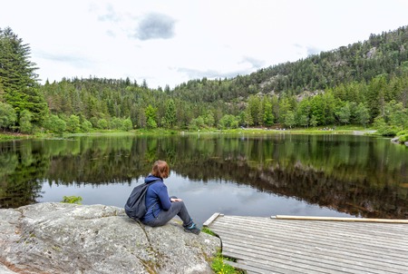 Alone young girl sitting and resting near by beautiful blue lake and clear big mountains. Original wallpaper from summer morningの写真素材