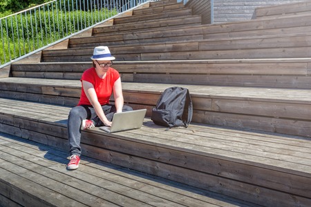 Girl with glasses lying on the wooden stairs and using laptop and typingの写真素材