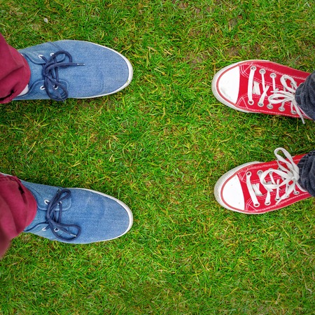 Red and Blue Sneakers shoes walking on grass concrete top view , Canvas shoes walking on concrete , two sneakers behind each others as a sign of love , Sneakers shoes Coupleの写真素材