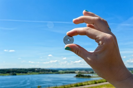 Hand making okay sign by holding a European coin, Norway seashoreの写真素材