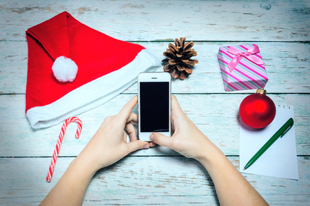 The famale hands with Christmas decorations. Phone, Santa hat, candy, ball, gift boxの写真素材