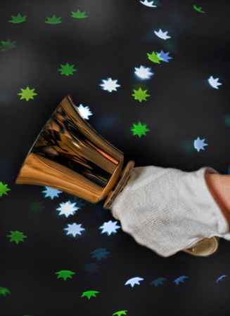 Jingle bells. Close-up of girl holding metal bell in hand and against light bokeh backgroundの写真素材