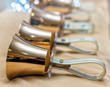 Jingle bells. Close-up of girl holding metal bell in hand and against light backgroundの写真素材