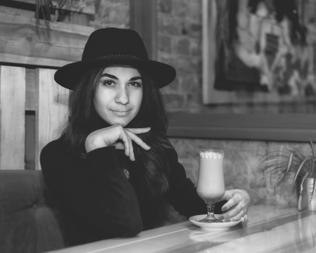 Beautiful young girl in hat drinking coffee in cafeの写真素材