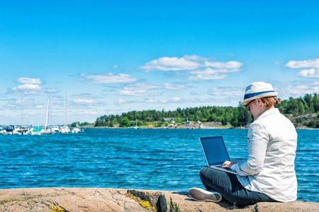 Profile of a self employed woman working with a laptop on the beach with the sea in the backgroundの写真素材