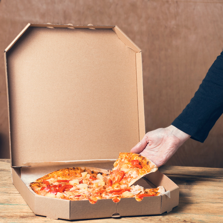 Female hands taking a slice of pizza from the box on the kitchen table, close upの写真素材