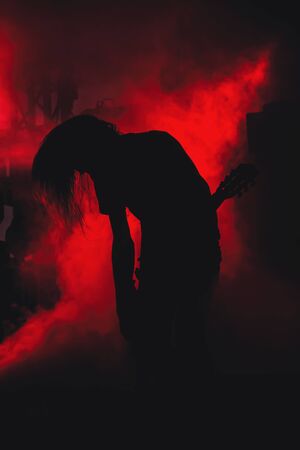 abstract composition with silhouette of guitar player on red light and smoke backgroundの写真素材