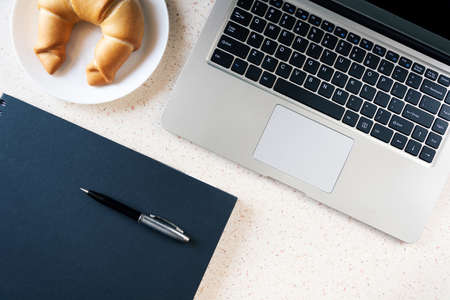 desktop with laptop notebook pen and plate with croissantの写真素材