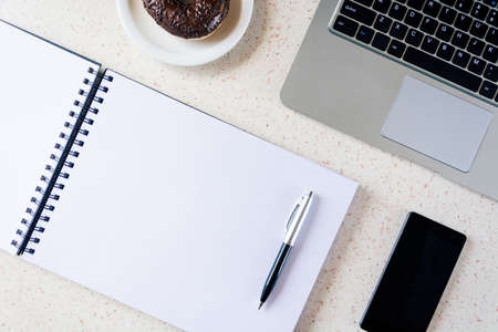 top of desk with notebook pen smartphone plate with donut and laptop keyboard home officeの写真素材