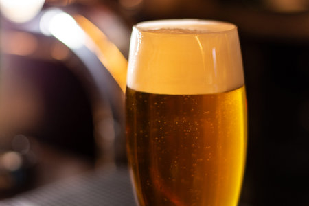 a glass of cold craft golden beer whit high foam closeup blurred background