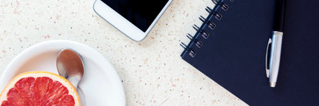top of the office desk with smartphone blue notebook pen and plate with spoon and grapefruit horizontal, panoramaの写真素材