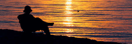relaxed man silhouette on orange sea background panoramaの写真素材