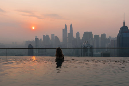 View of Kuala Lumpur City from roof top swimming pool at sunrise. Girl in the pool overlooking the...