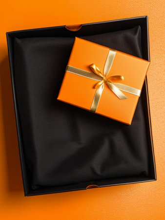 Gift box with golden bow on orange background. Top view.の素材
