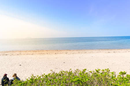 Two unidentified people are setting at the beach. Fresh air, blue sky sunlight, chilling out, and relaxing on holidayの写真素材