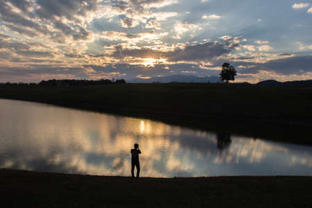 Silhouette of a photographer in front of lake at sunset timeの写真素材
