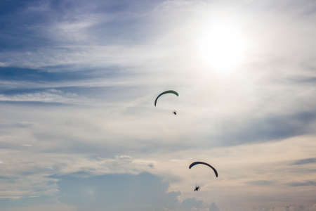 Silhouette men flying with paramotor in the blue sky backgroundの写真素材