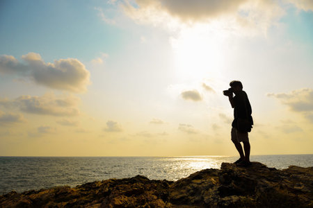 Silhouette of photographer taking photo on the top of mountaing before sunsetの写真素材