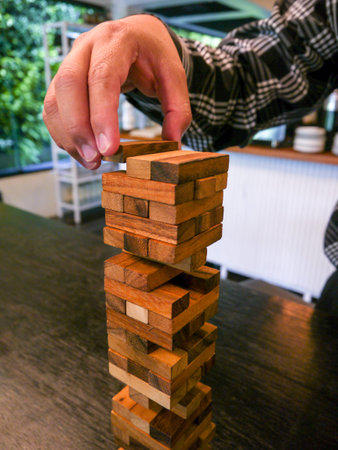 A man playing Jenga game or wooden block tower game. Playing game in coffee shop. Skill development...
