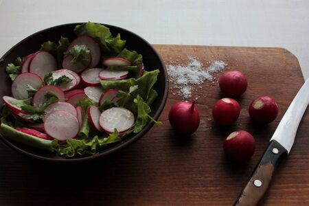 Fresh radish, lettuce and parsley salad in a brown ceramic bowl on a wooden cutboardの写真素材