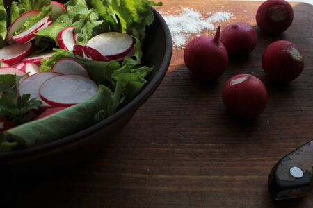 Fresh radish, lettuce and parsley salad in a brown ceramic bowl on a wooden cutboardの写真素材