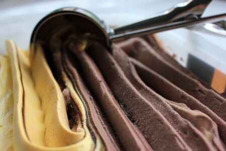 Scoop ice creame process. Textured orange and chocolate ice cream in a plastic box on white background with copy space. Selective focusの写真素材