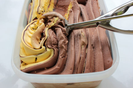 Scoop ice creame process. Textured orange and chocolate ice cream in a plastic box on white...