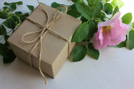 Brown craft gift box decorated with pink wild rose hips flower on old wooden background with copy...