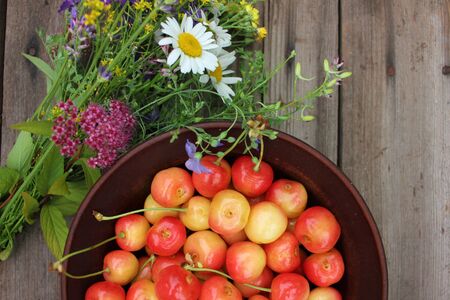 Yellow and pink cherries in a bowl, and midsummer wild flowers on a vintage wooden board background.の写真素材