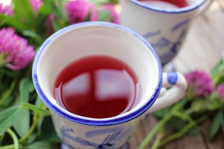Two cups of healing herbal tea or infusion with red clover, purple flowers on the wooden table. Natural floral background. Top viewの写真素材