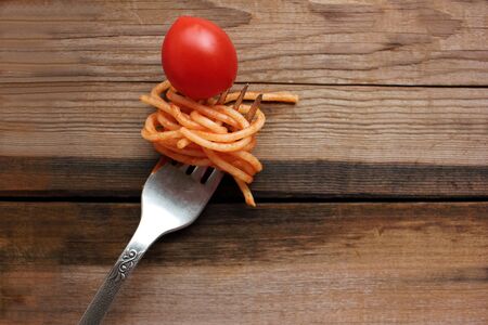 Spaghetti with tomato sauce and cherry tomato on a fork. Rustic wooden table background. Top view, copy spaceの写真素材