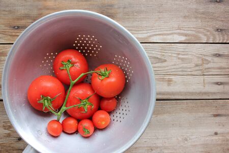 Fresh tomatoes on the vine and cherry tomatoes in the colander on rustic wooden table. Top view. Copy spaceの写真素材