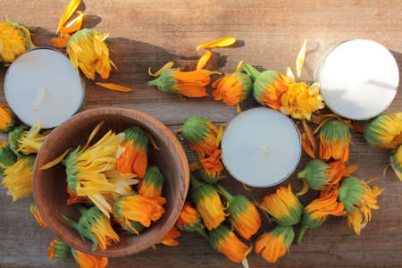Calendula officinalis flowers in a wooden bowl on the board background, and tea light candles. Close-up, copy space. Medicinal plant. Selective focus. Spa conceptの写真素材