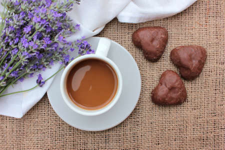 Cup of coffee with lavender flowers and chocolate heart shaped cookies on burlap texture. Top viewの写真素材