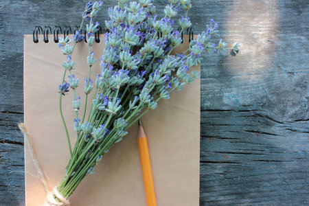 Open sketchbook with blank brown paper and a bunch of lavender flowers on rustic gray wooden...