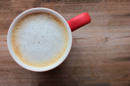 Red cup of coffee with milk or cappuccino on wooden table background with copy space. Enjoying morning coffee. Top view. Selective focusの写真素材