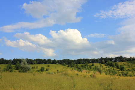 Idyllic summer landscape with green hills, trees, blue sky and clouds
