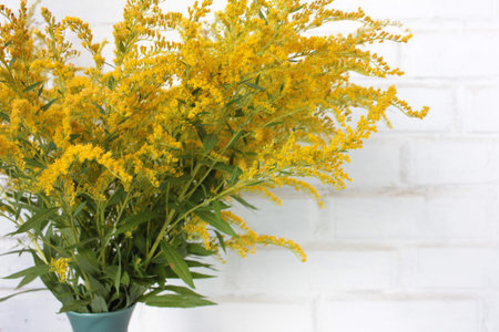 Bouquet of yellow flowers in vase on the white brick wall background. Autumn still life