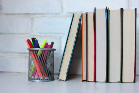 Stack of books and felt-tip pens on the table against white brick wall. Back to school background. Copy spaceの写真素材