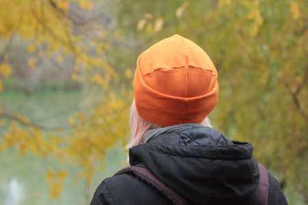Young woman in bright orange hat on the river and yellow leaves background. Golden autumn landscapeの写真素材