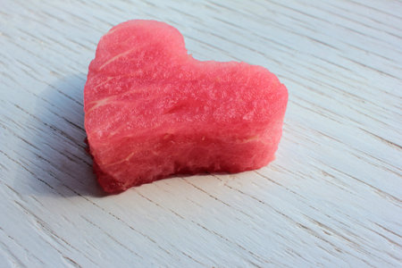 Red heart on wooden table. Heart-shaped slice of watermelon on white background. Top view, copy spaceの写真素材